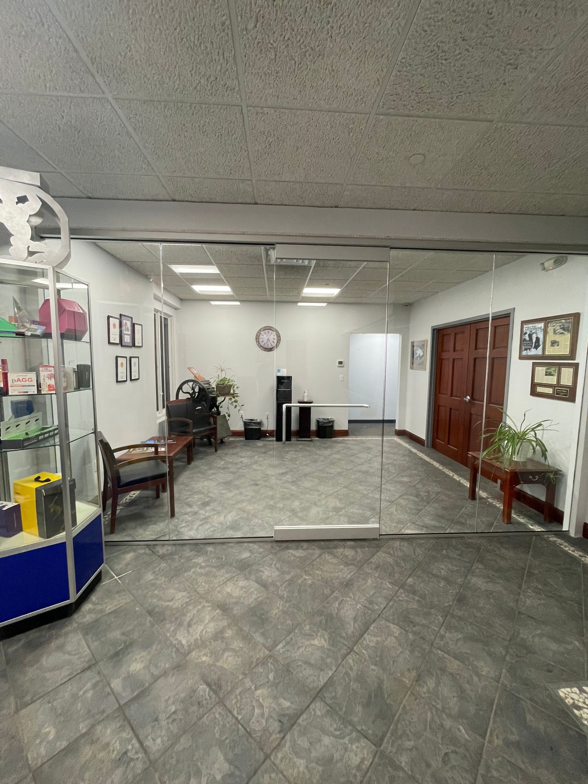 Interior of a shop with display case, seating, and a doorway. Gray tiled floor, white walls, and wood doors.