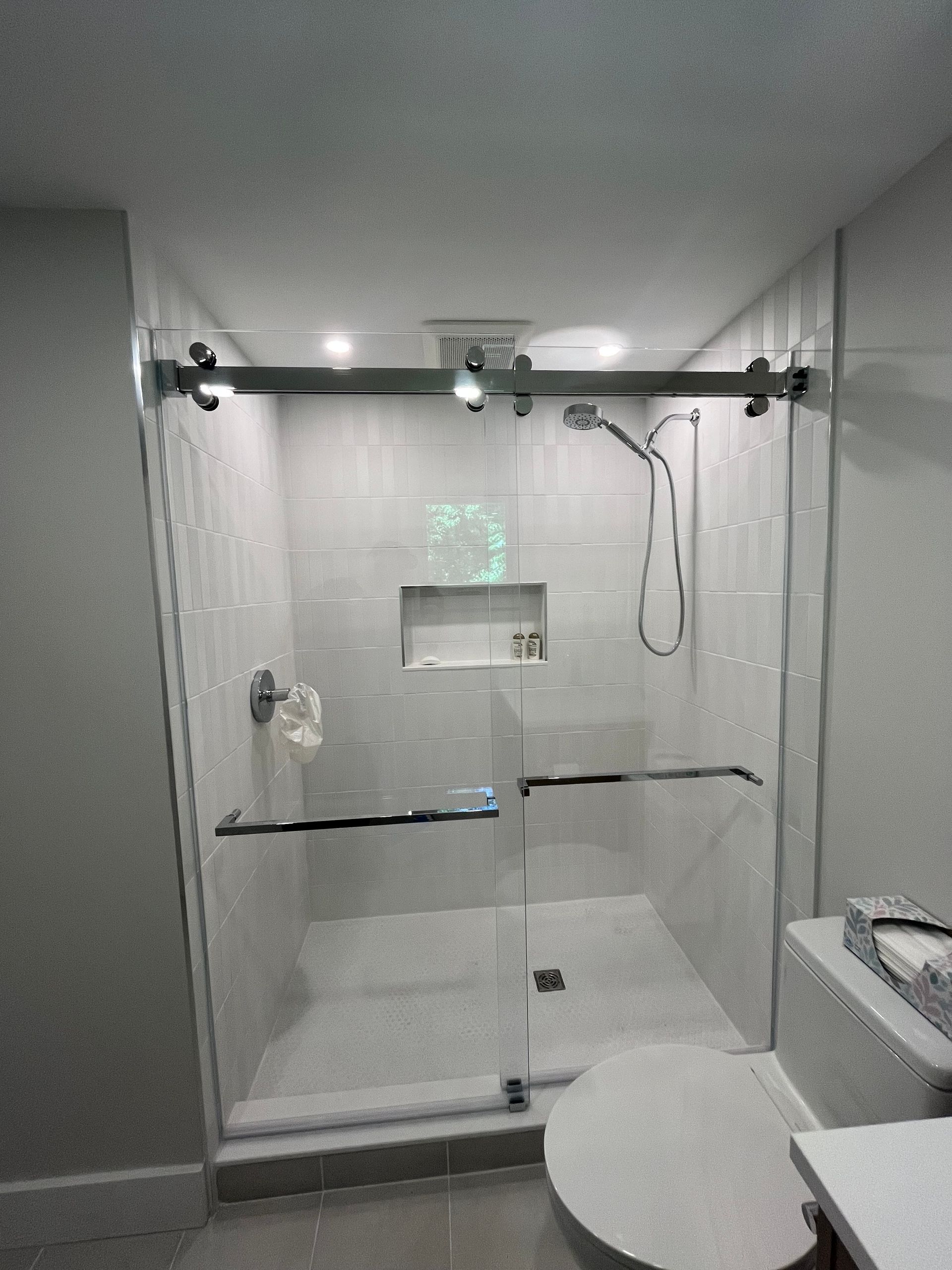 Modern bathroom shower stall with sliding glass door, white tiles, and chrome fixtures.