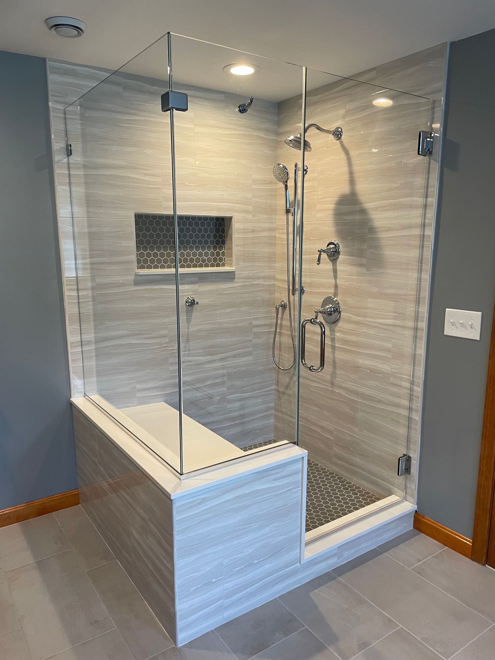 Modern shower with glass doors, built-in bench, and gray tile walls and floor.