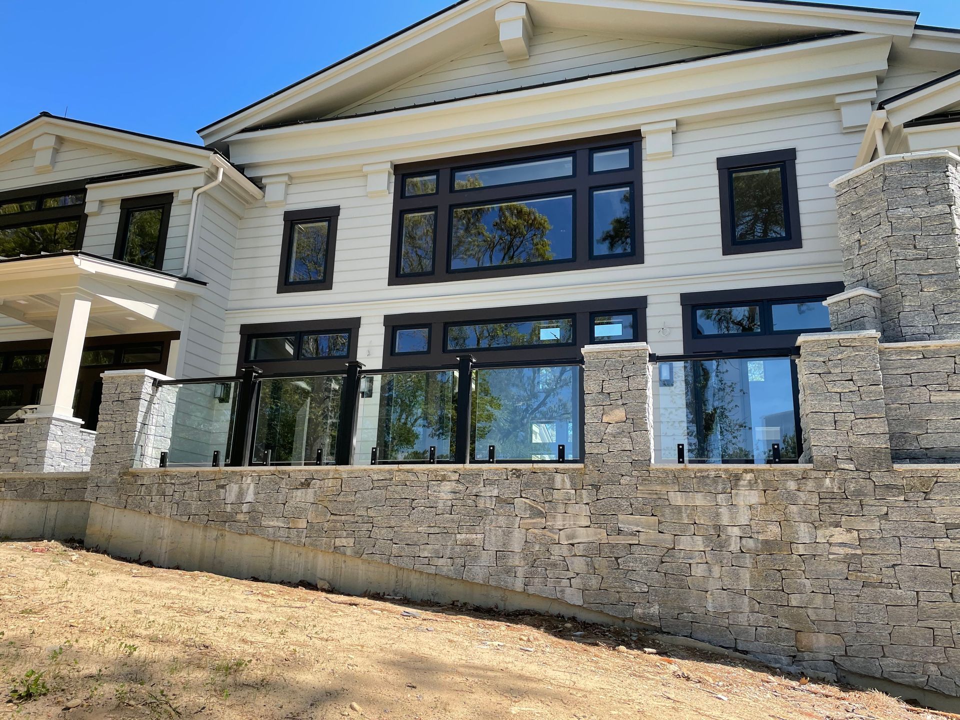 White house with dark window frames, glass railing on stone wall, and blue sky.