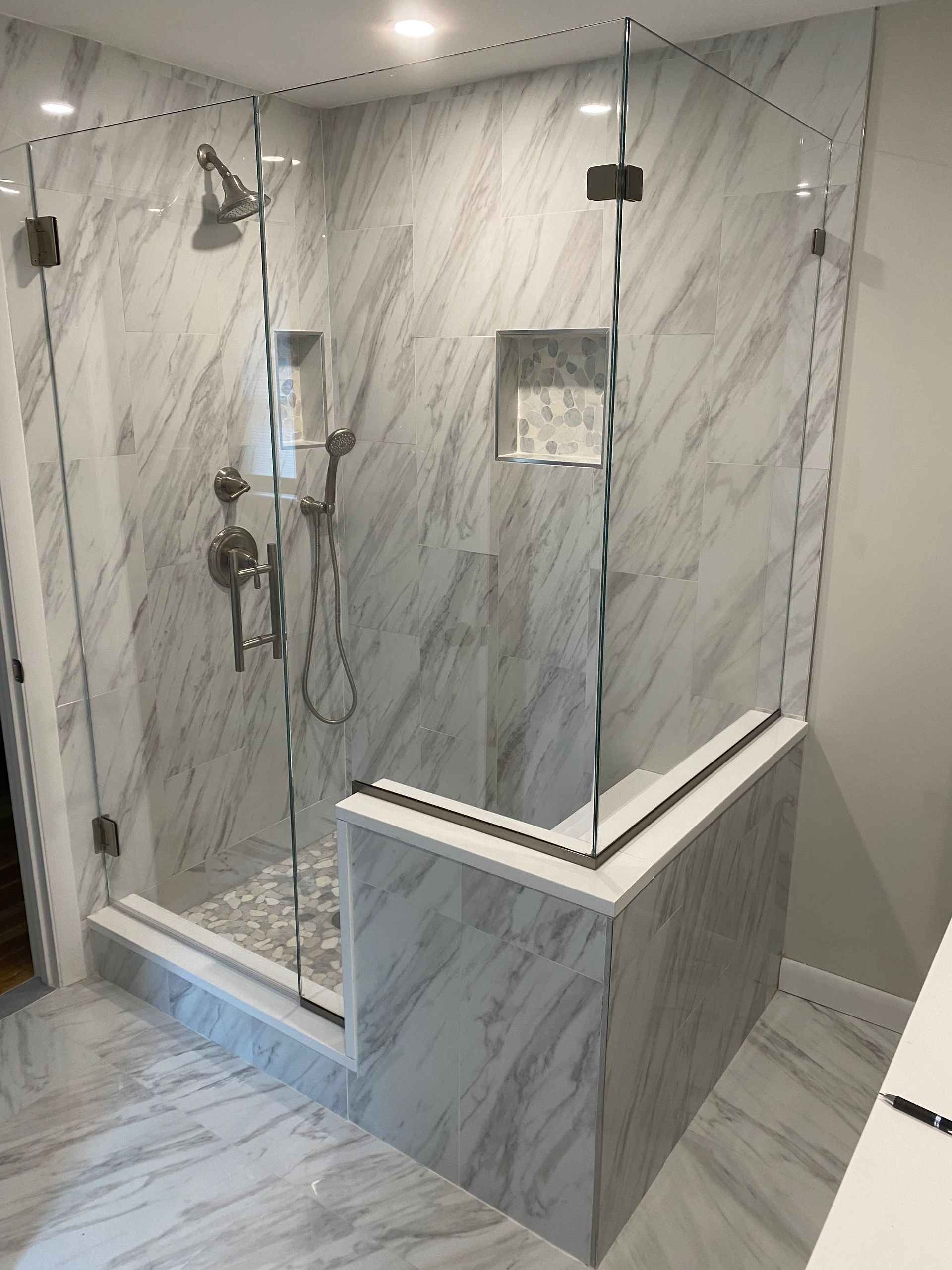 Modern bathroom with marble tiles, glass shower enclosure, and chrome fixtures.