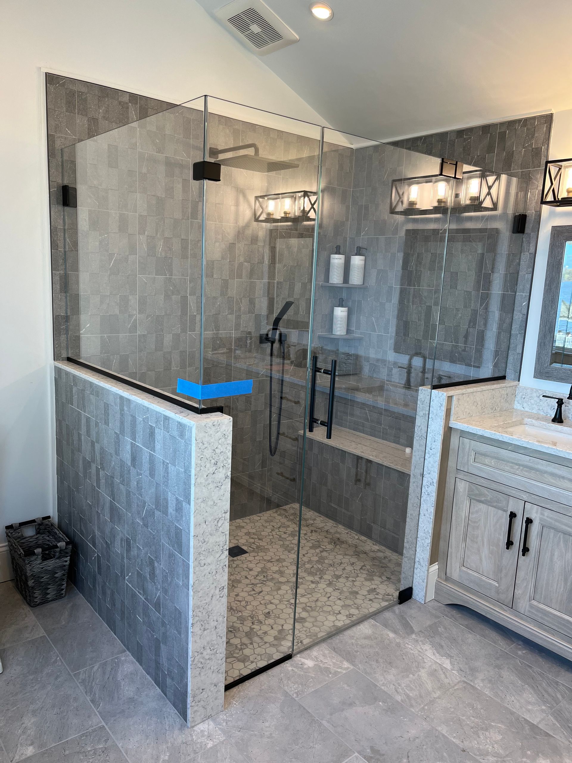 Modern gray-tiled walk-in shower with glass doors, black hardware, and a vanity.