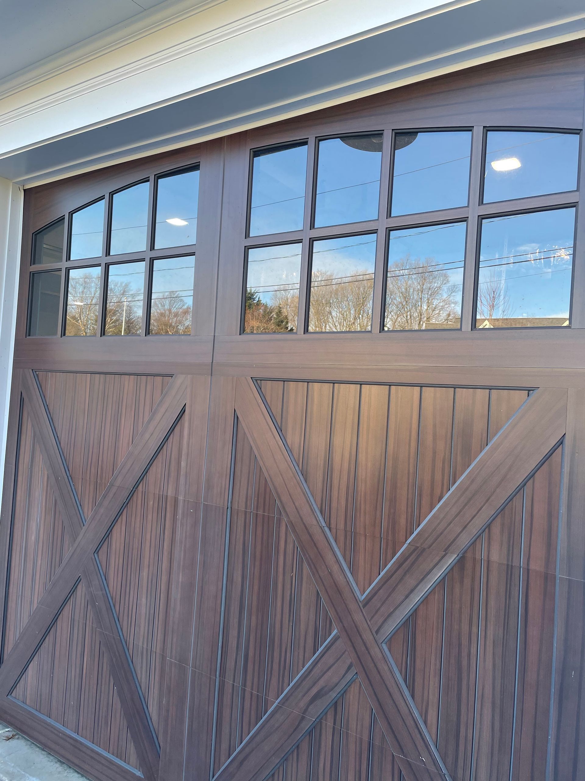 Wooden garage door with glass panel windows reflecting a bright sky.