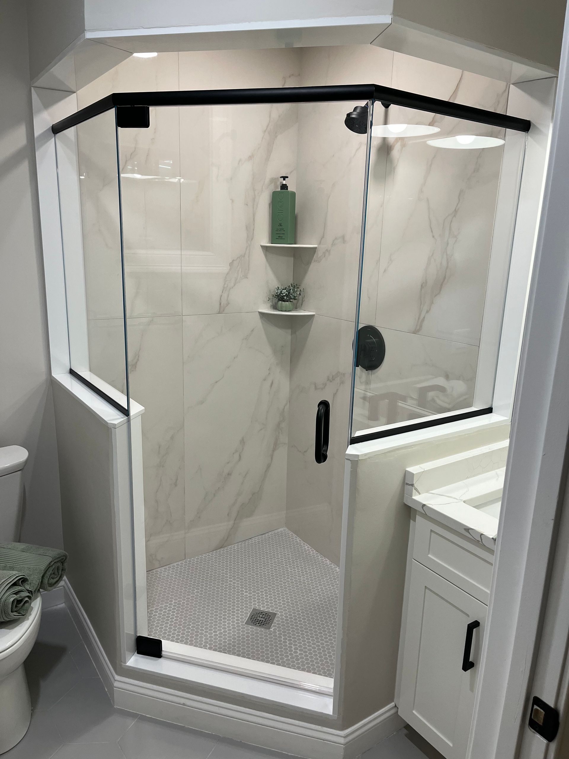 Angled glass shower enclosure with white tile and black trim.