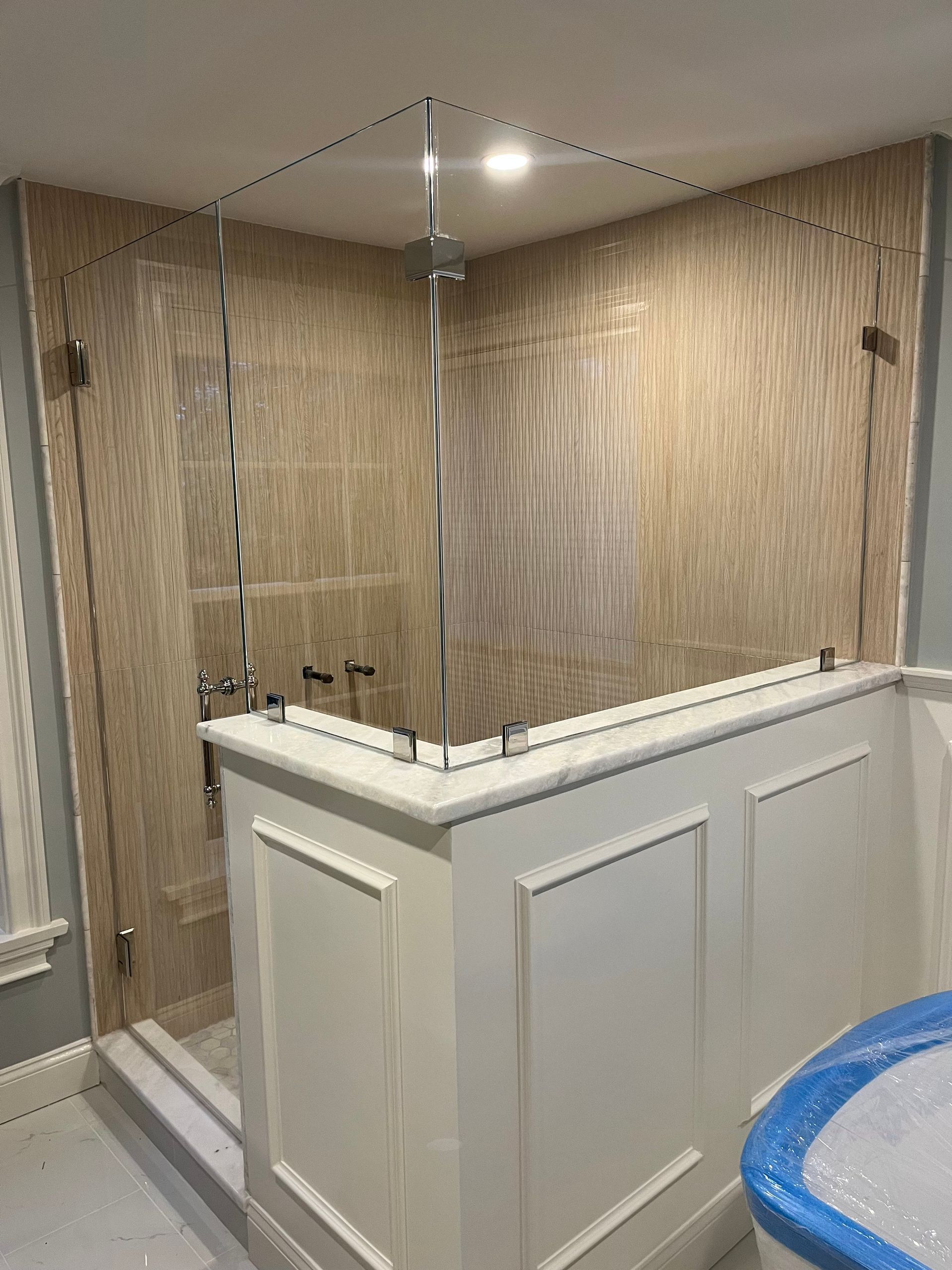 Shower enclosure with glass panels, beige tile walls, and white wainscoting.
