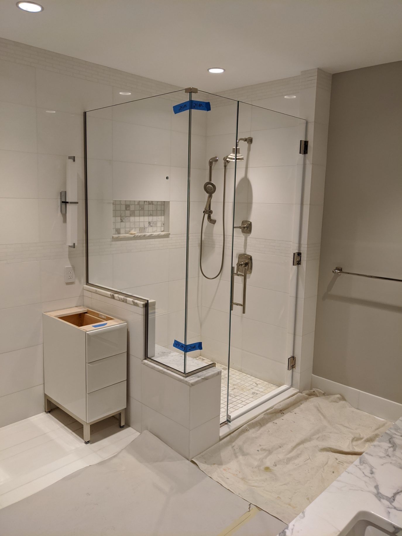 New glass shower enclosure with white tile walls and shower fixtures.