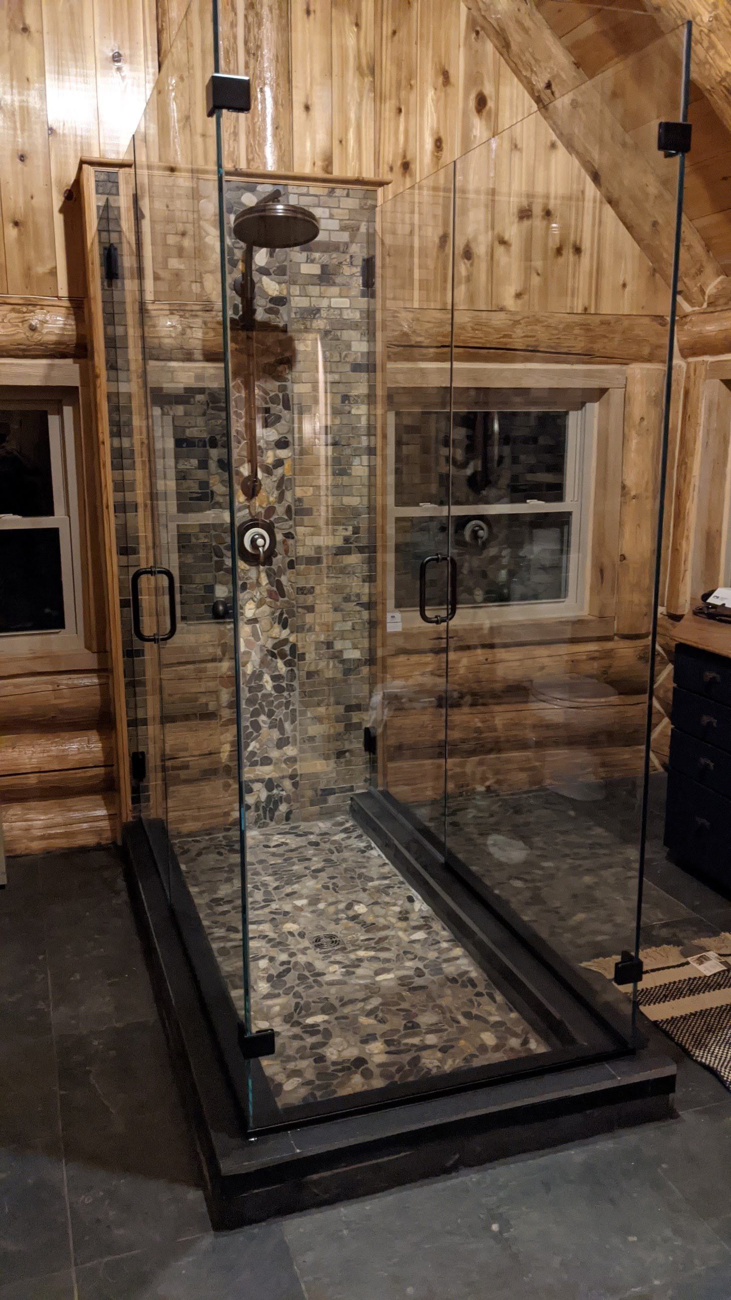 Glass shower with stone backing in a rustic wooden cabin.