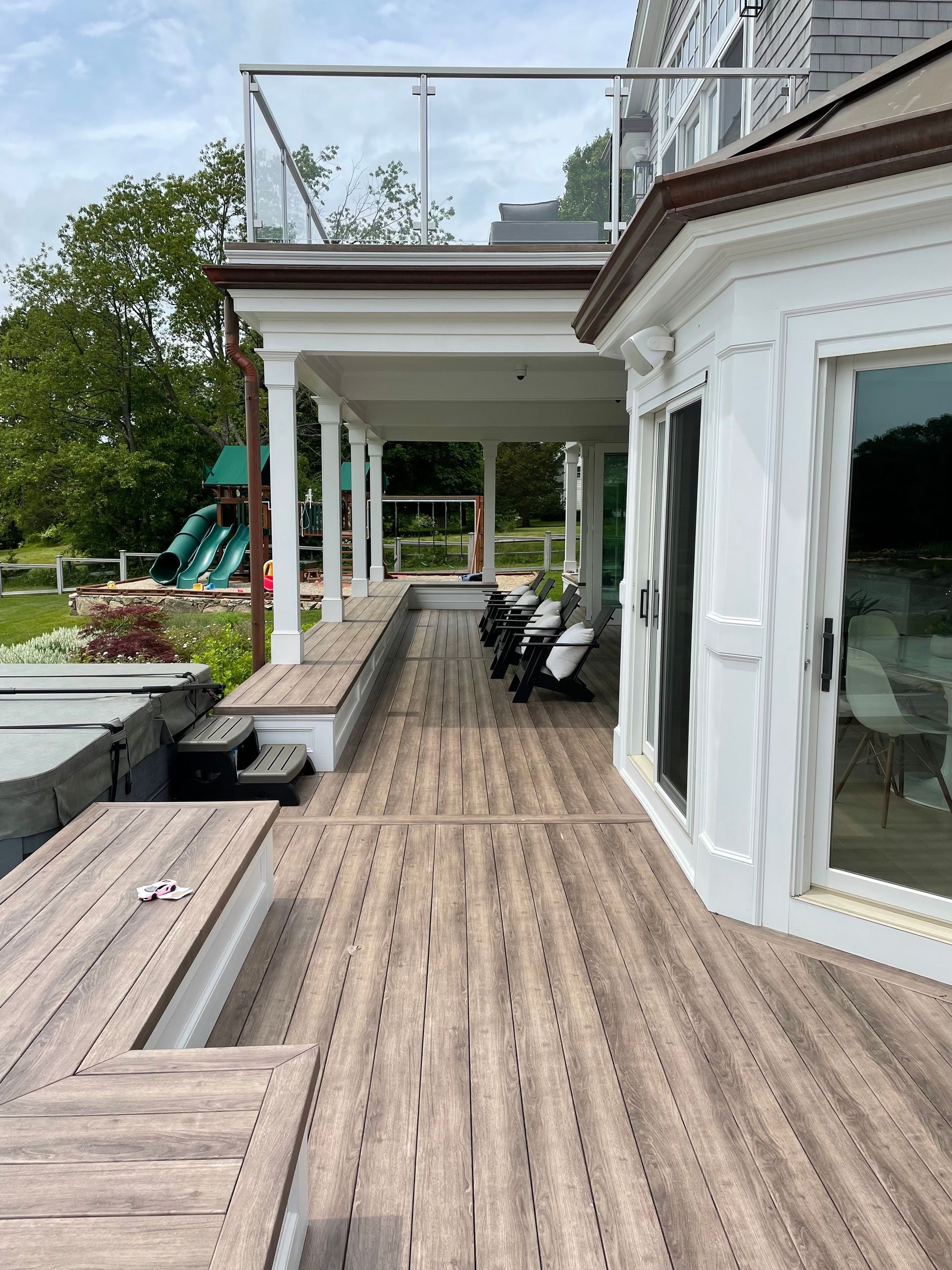 Wooden deck with covered porch and glass railing on a waterfront property.