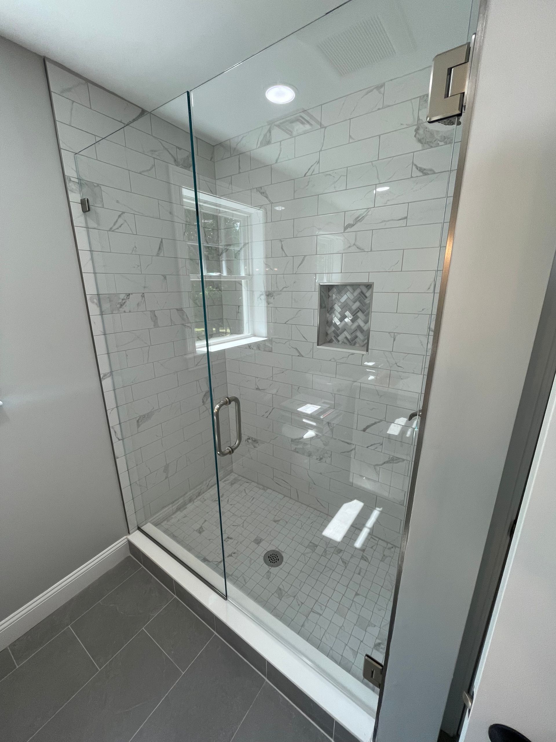 Glass-enclosed shower in a modern bathroom with marble-look tile walls and gray floor tiles.