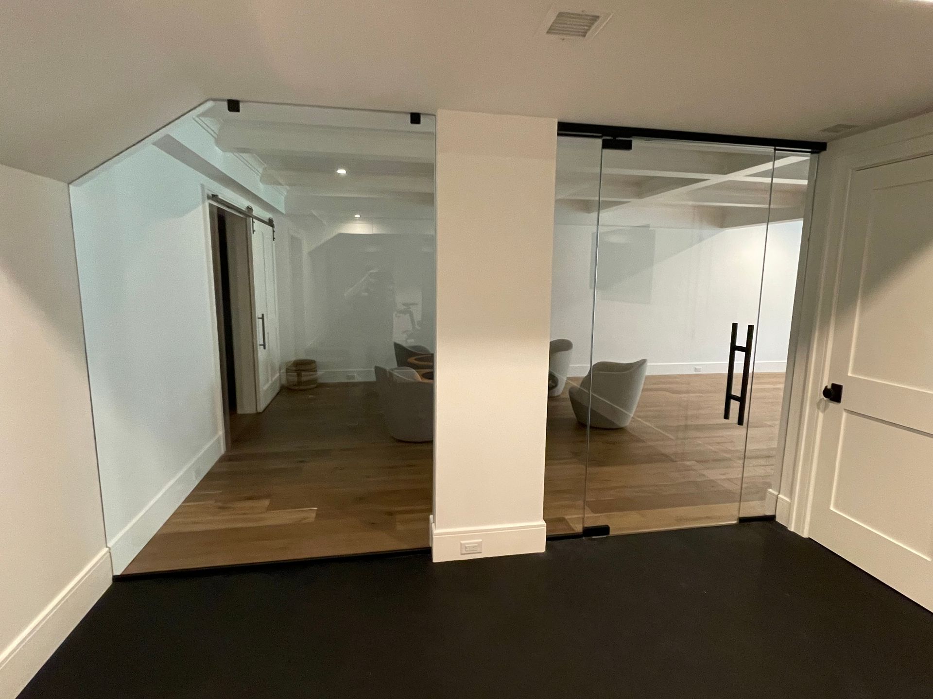 Glass-walled room with wooden floors, white walls, and black trim. Sliding glass doors with black hardware, two armchairs inside.