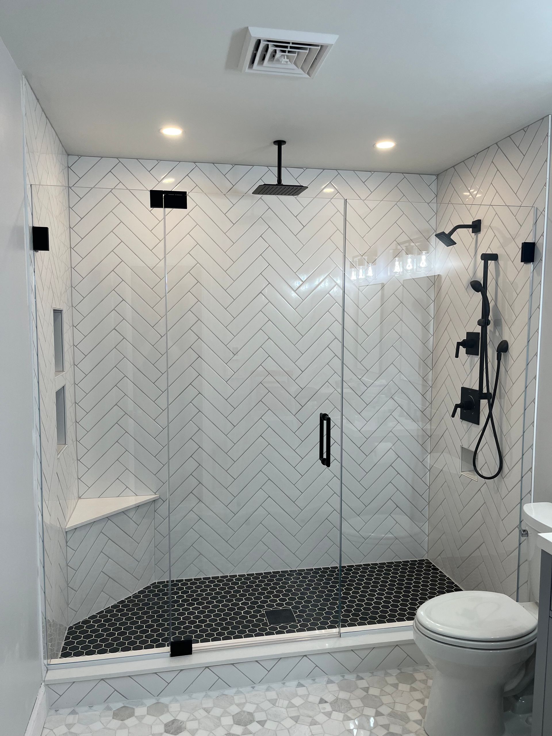 Shower with black and white herringbone tile, glass doors, and pebble floor.