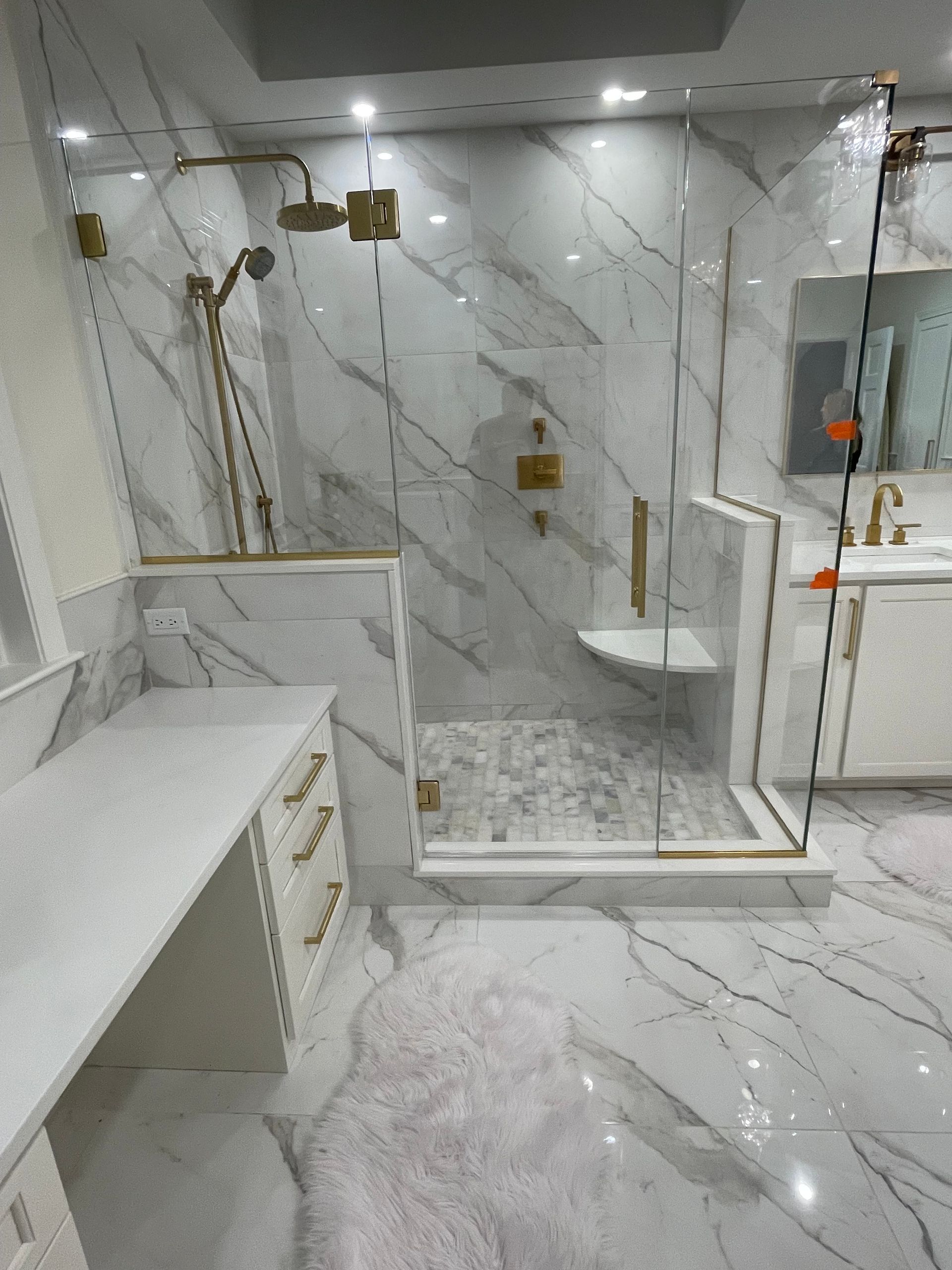 Luxurious marble-tiled bathroom with a glass shower, gold fixtures, and white vanity.