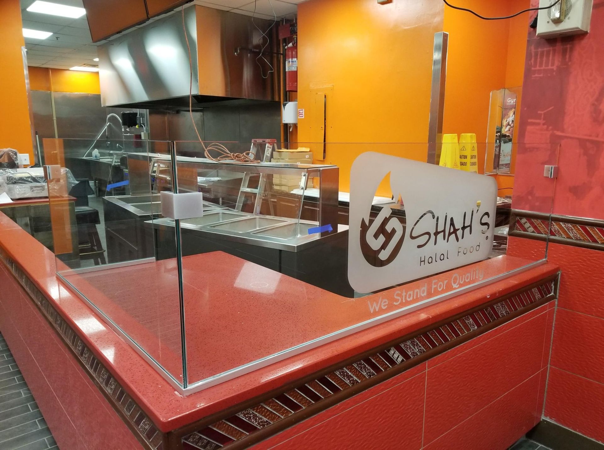 Interior of Shah's Halal food counter, orange and red color scheme. Sign and glass food display, food prep area in the background.
