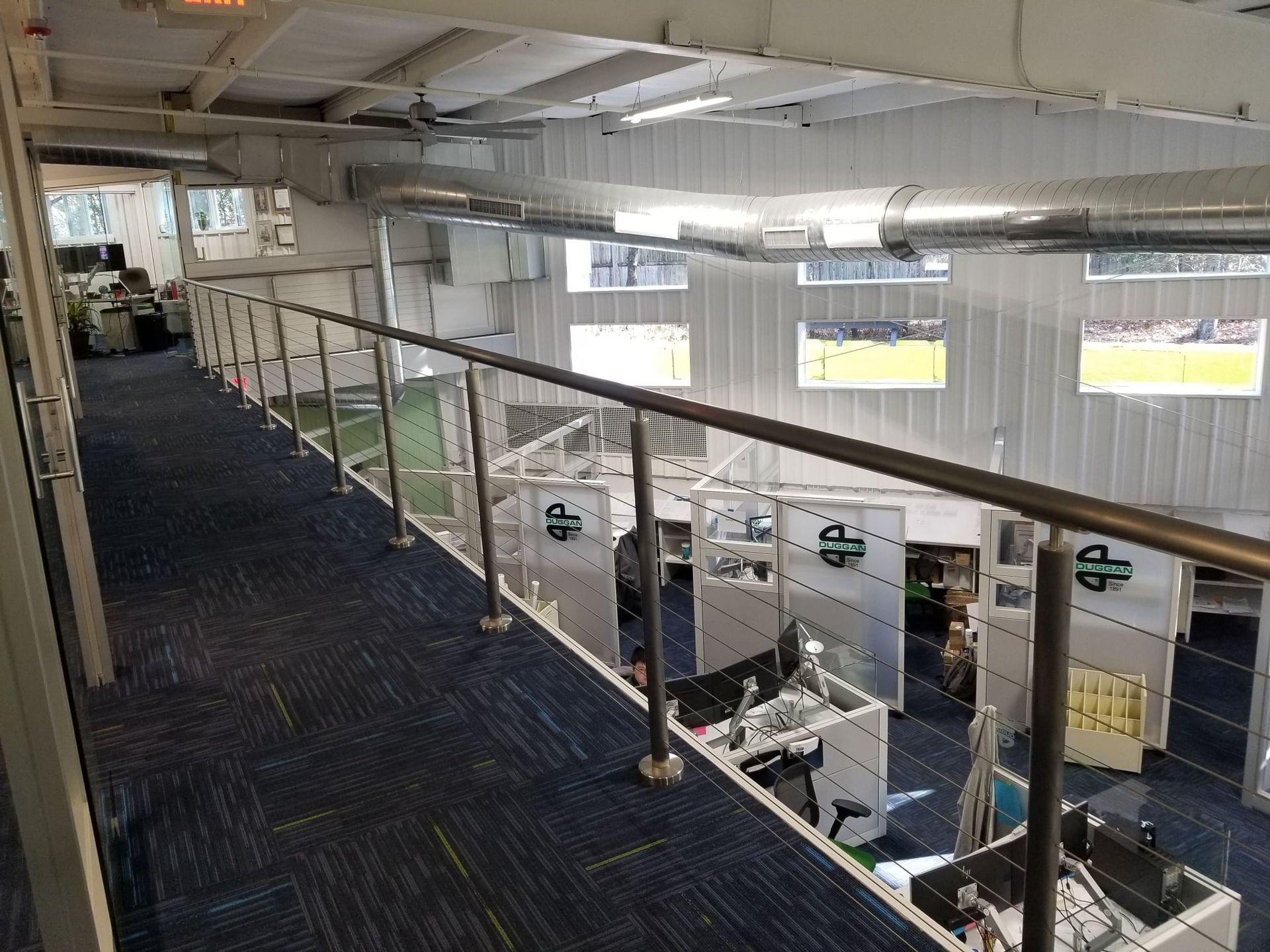 Overhead view of a modern office space with a walkway, glass railing, and workstations below.