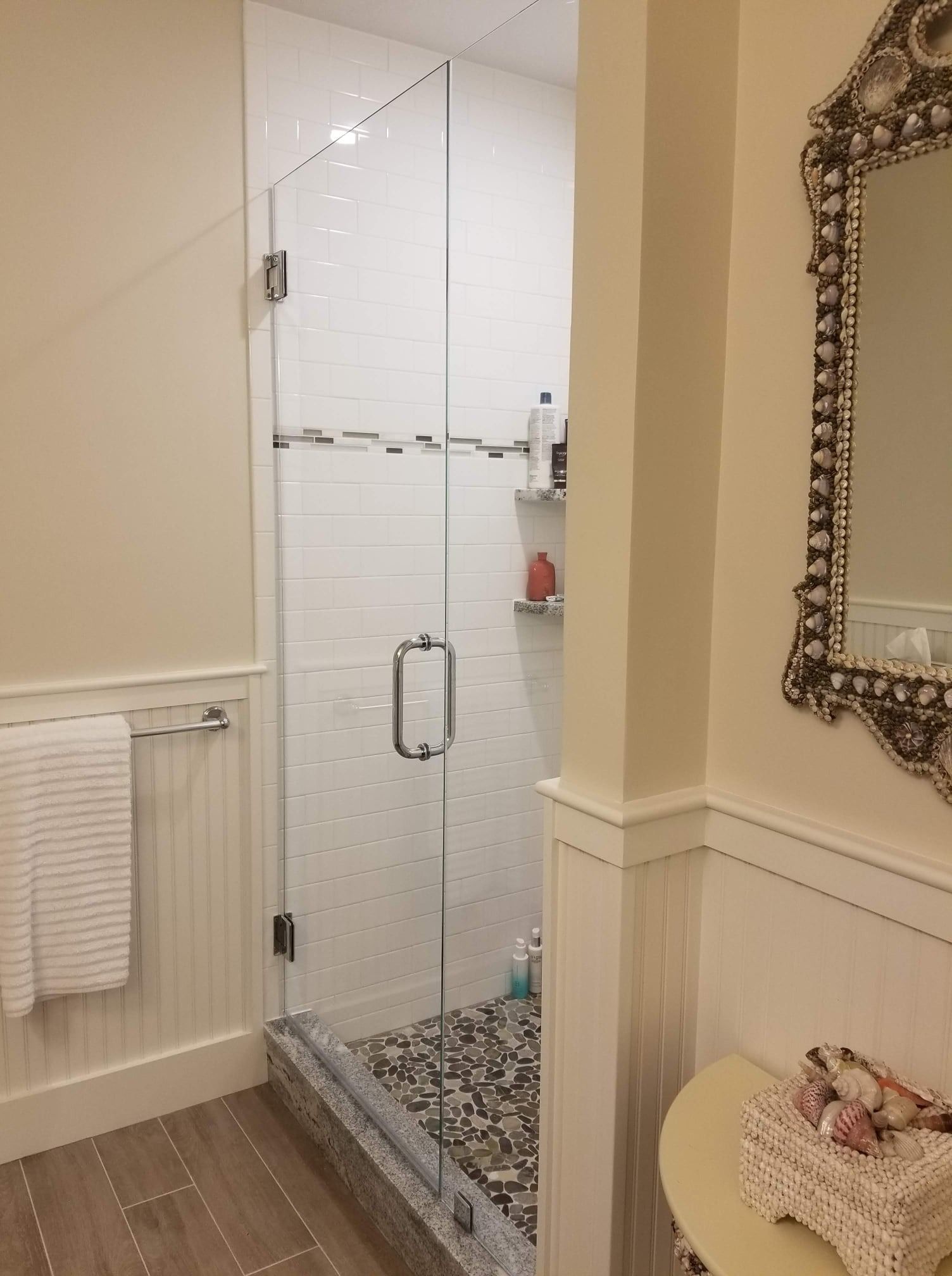 Glass shower enclosure with gray pebble floor, white tiled walls, and towel rack.