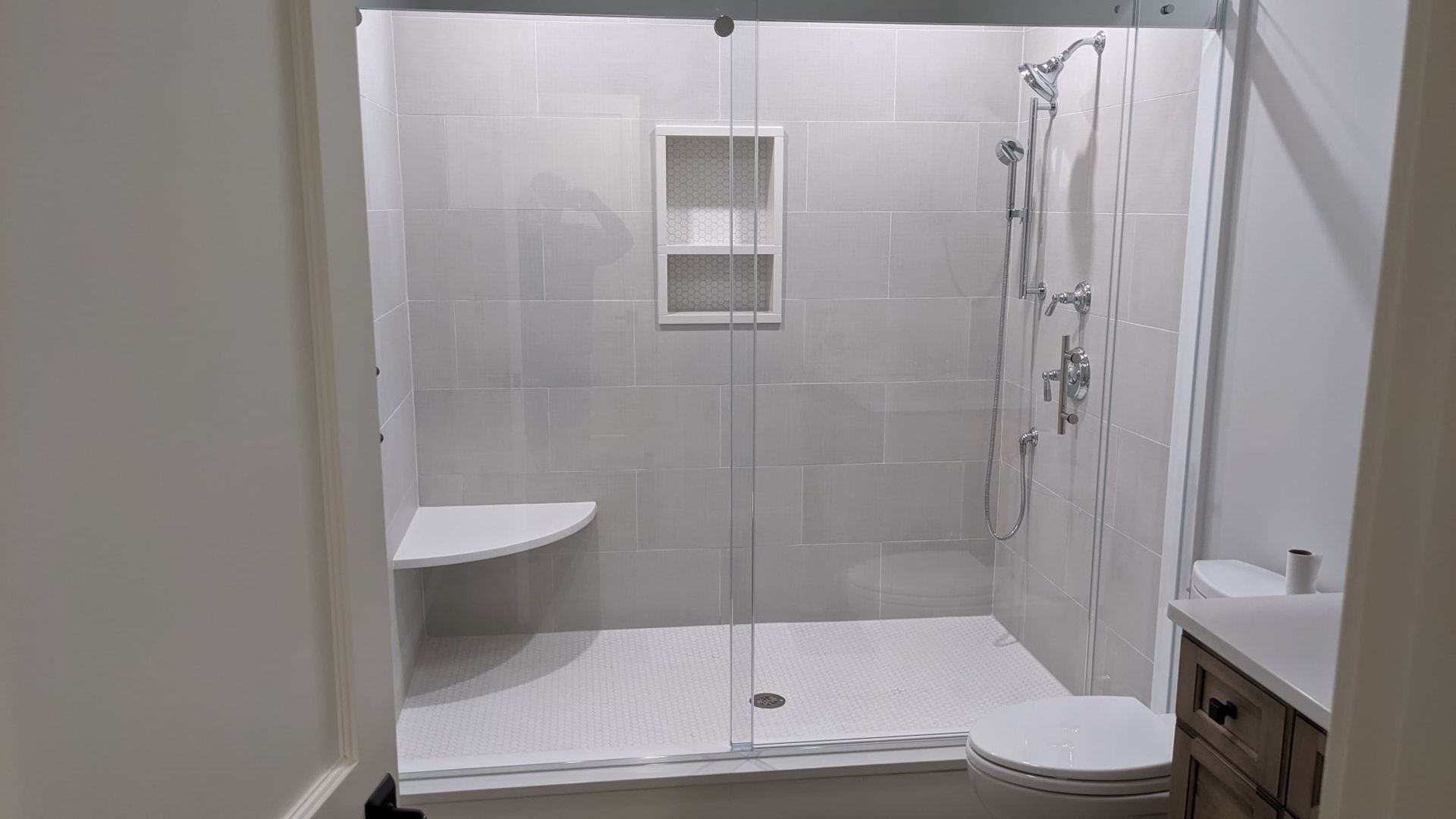 A modern bathroom shower with glass doors, tiled walls, and built-in shelving and bench.