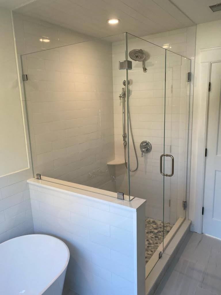 Modern bathroom with glass shower enclosure, white tile walls, and pebble flooring.