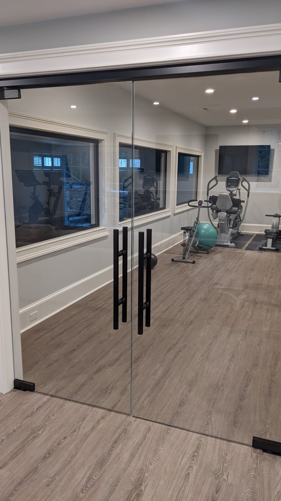 Glass door leading into a home gym with workout equipment and windows.