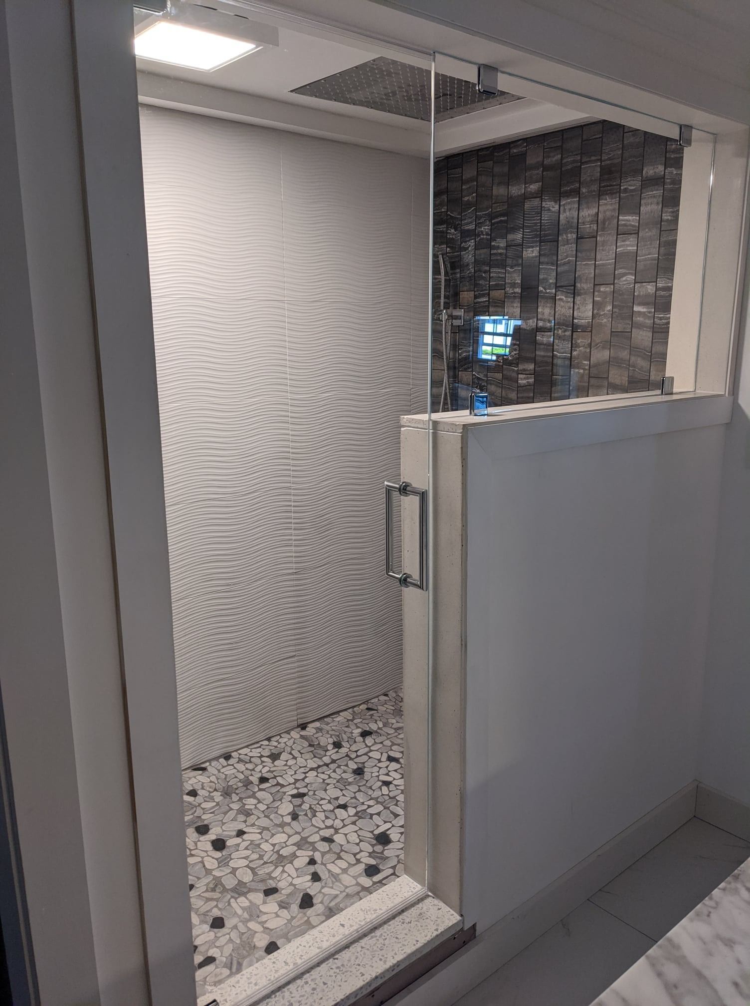 Shower with glass door, pebble floor, white and textured walls, and a stone accent wall.