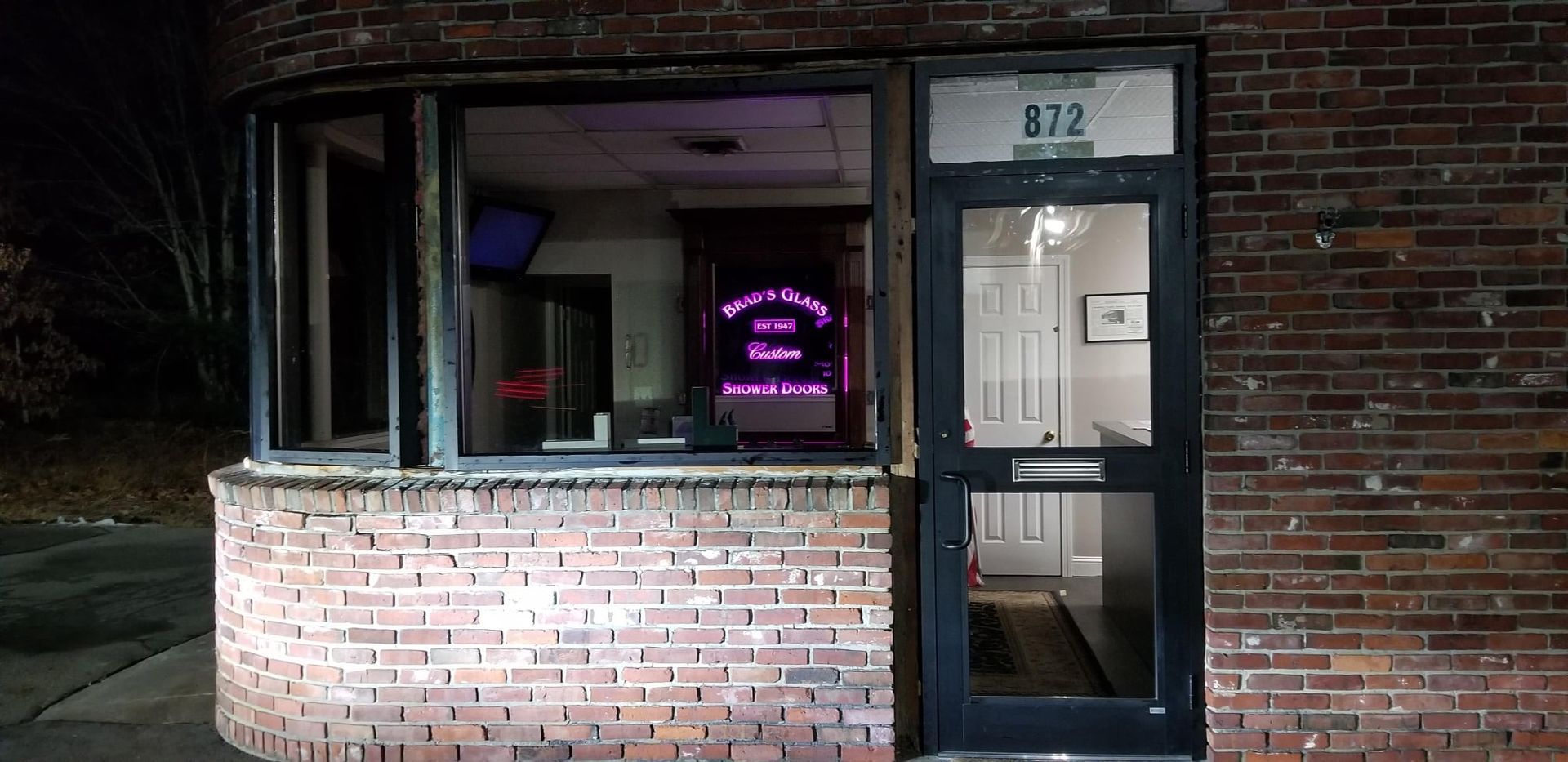 Exterior of a brick building at night. A business entrance has glass door with 