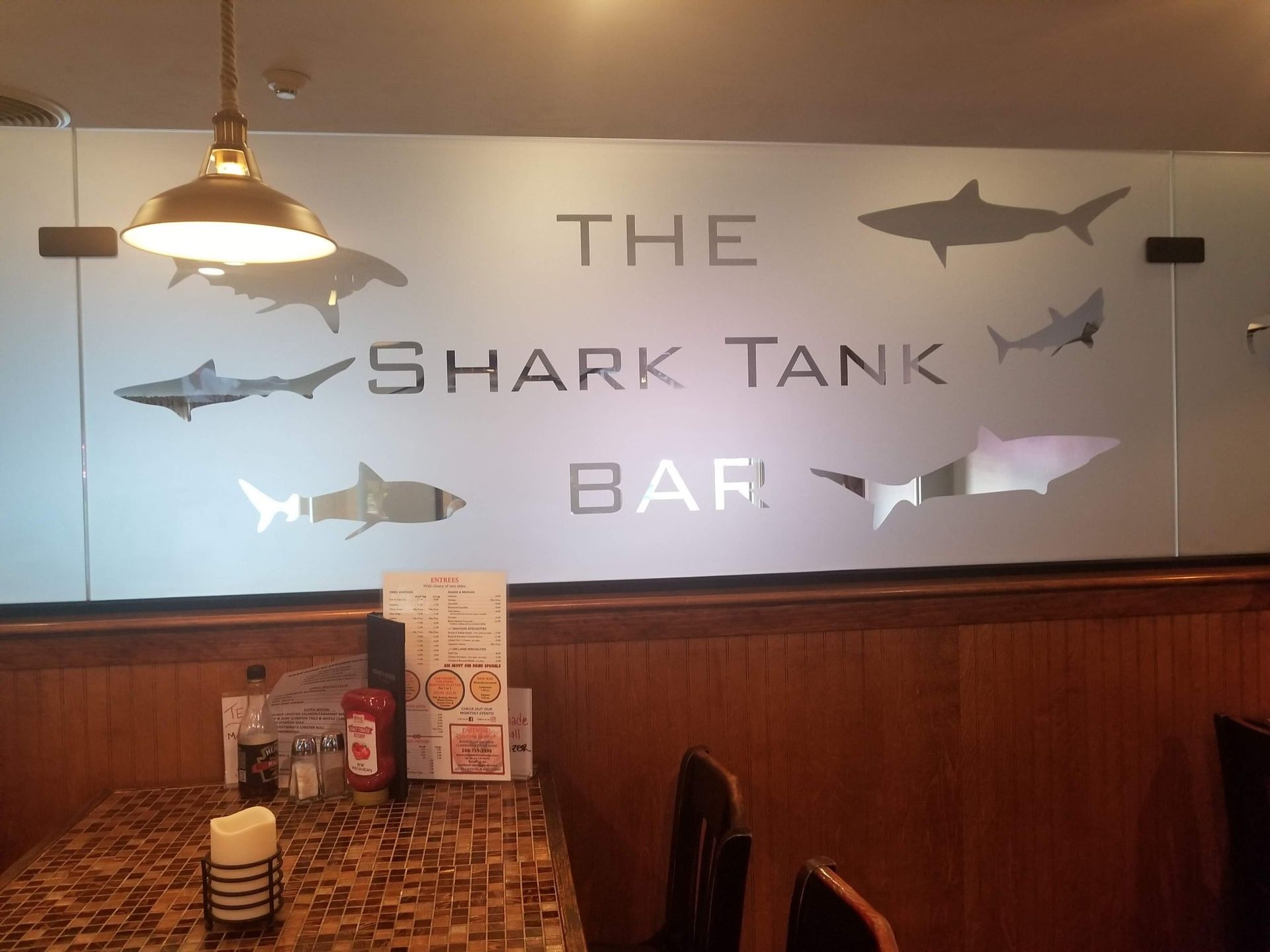 The Shark Tank Bar sign with shark silhouettes on a window above a table set for dining.