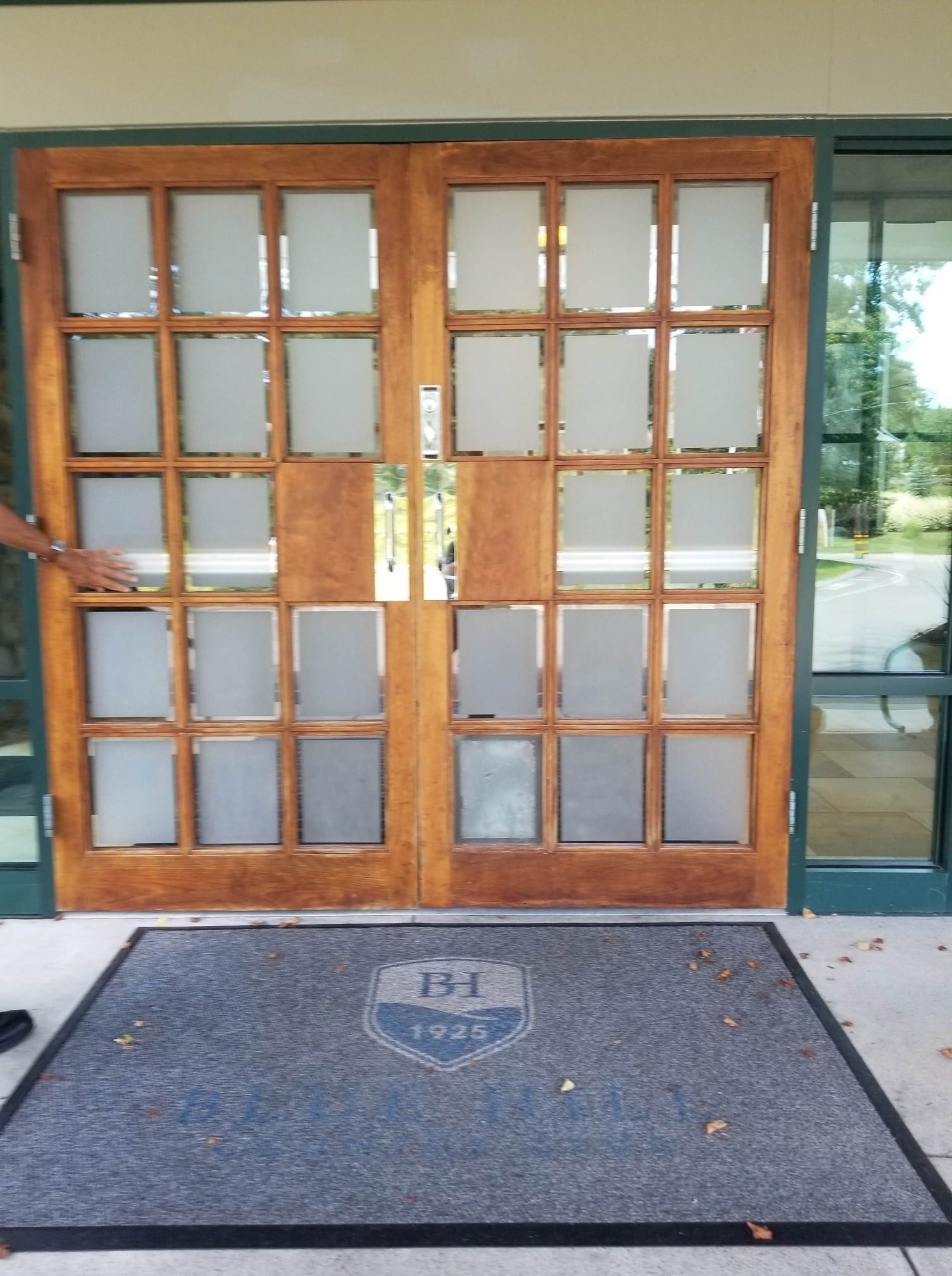 Two wooden doors with frosted glass panels, an entrance mat, and a person opening the door.