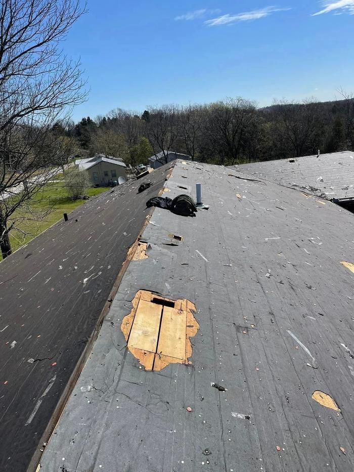 Damaged shingle roof with visible wood underlayment; residential setting, sunny day.