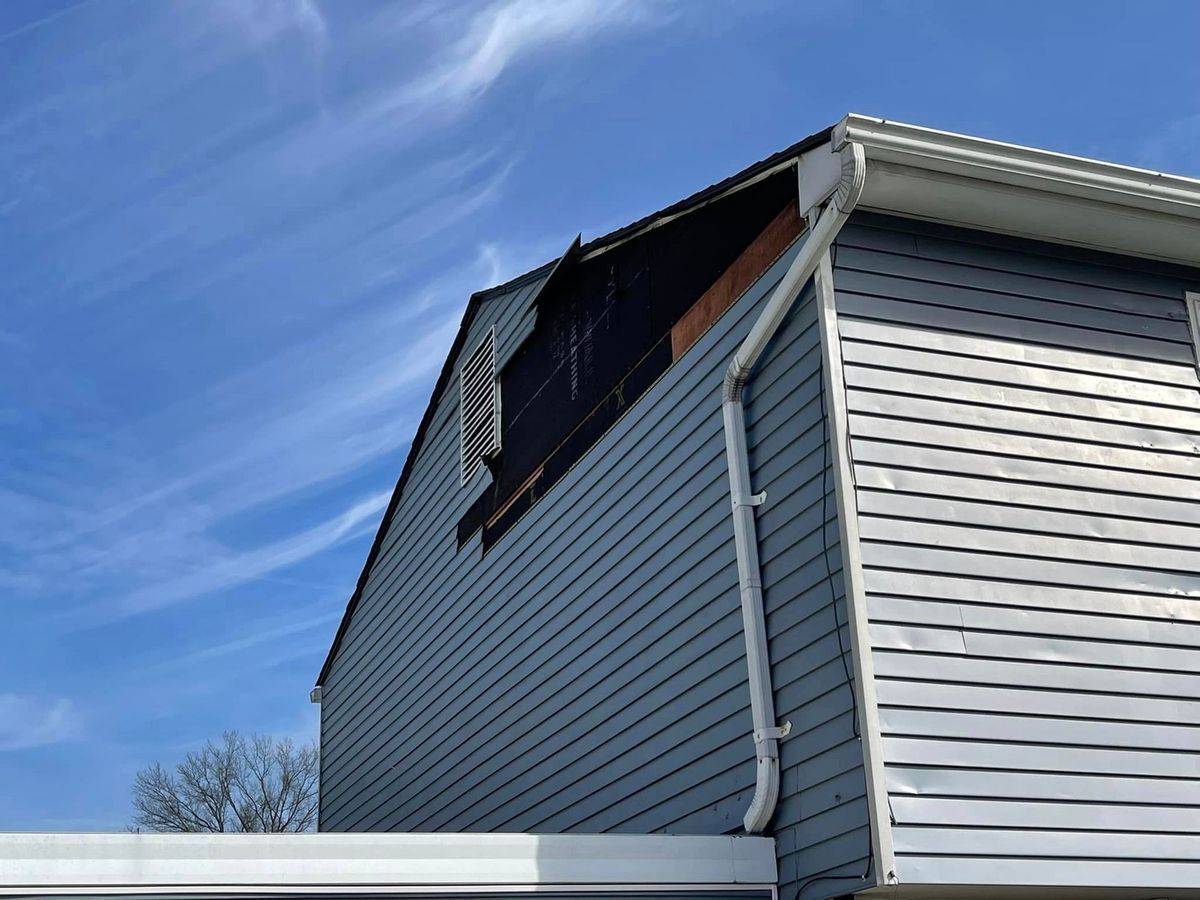 Exterior view of a house with visible fire damage on the roof and siding. The sky is blue.