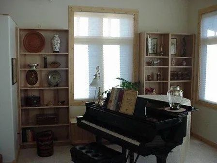 A piano is sitting in a living room surrounded by shelves and windows.