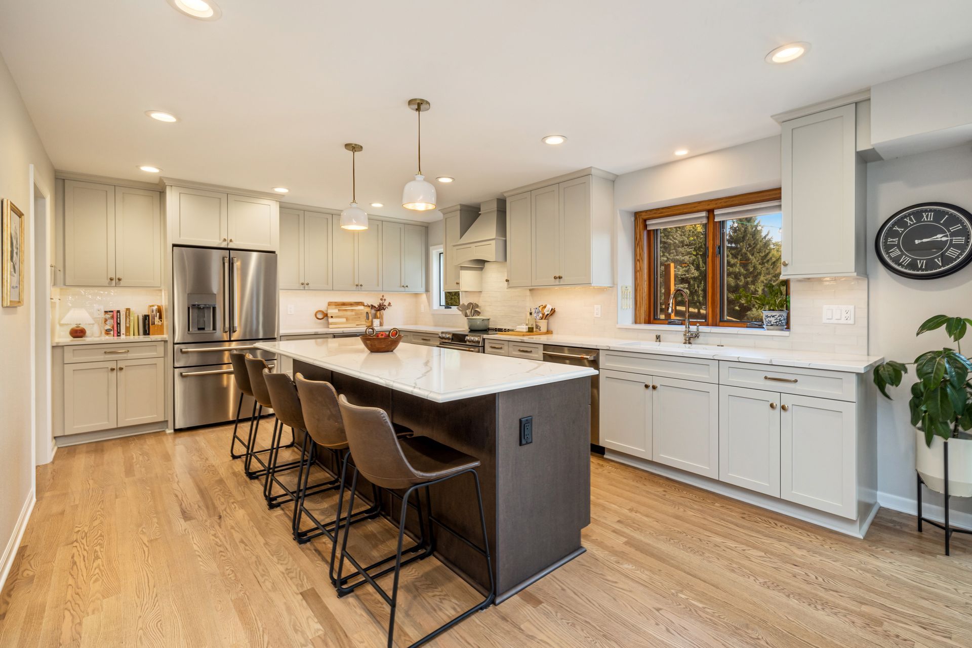 A kitchen with white cabinets, stainless steel appliances, a large island, and a clock on the wall.