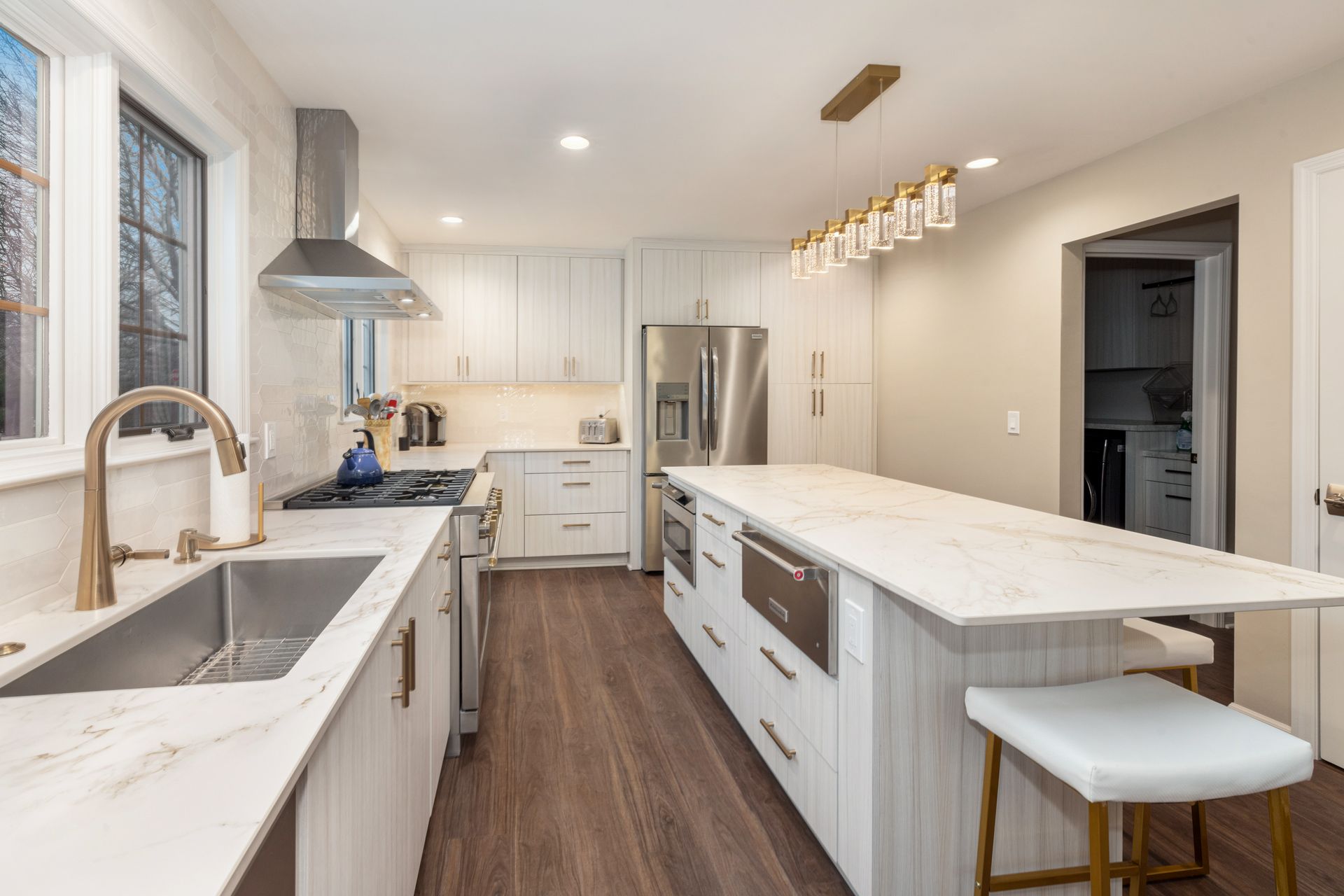 A kitchen with white cabinets, stainless steel appliances, a large island, and a sink.