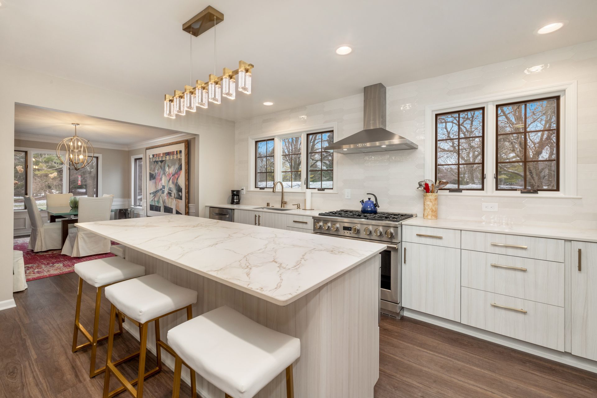 A kitchen with white cabinets, marble counter tops, stainless steel appliances, and a large island.