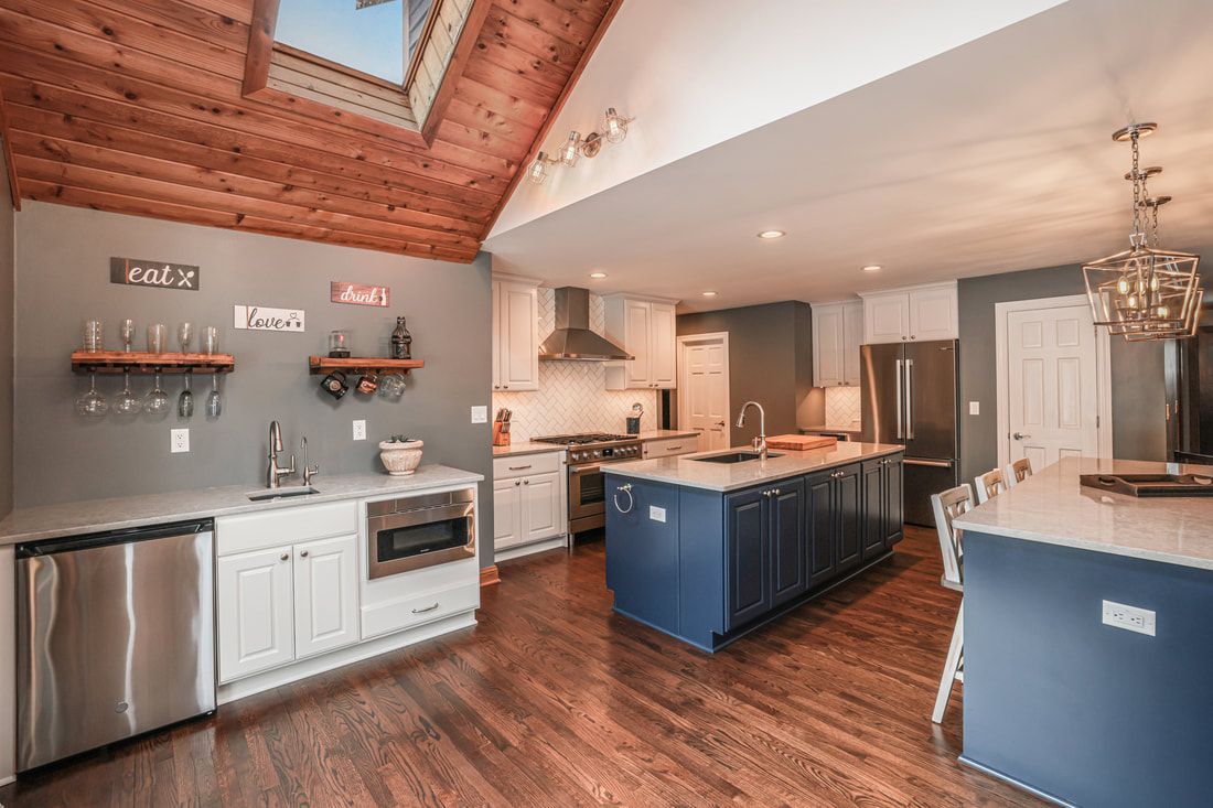 A kitchen with blue cabinets , white cabinets , stainless steel appliances , hardwood floors and a skylight.
