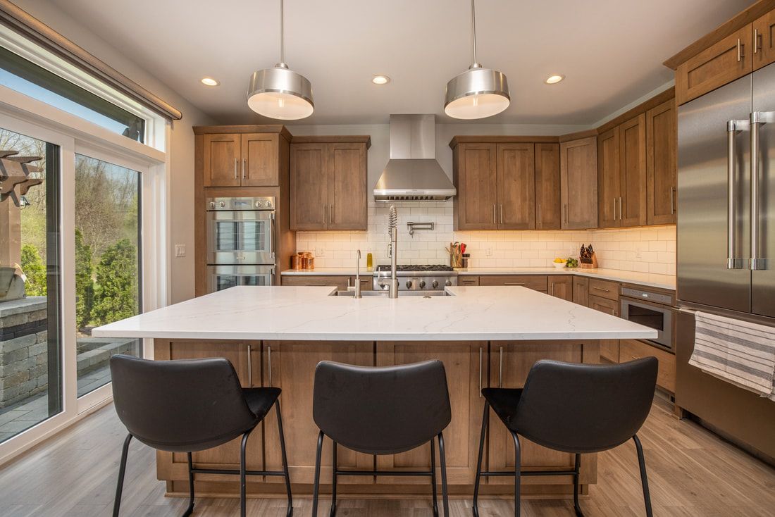A kitchen with stainless steel appliances , wooden cabinets , a large island , and three chairs.