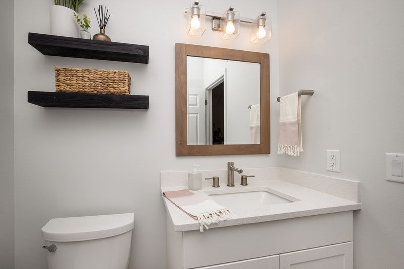 A bathroom with a sink , toilet , mirror and shelves.