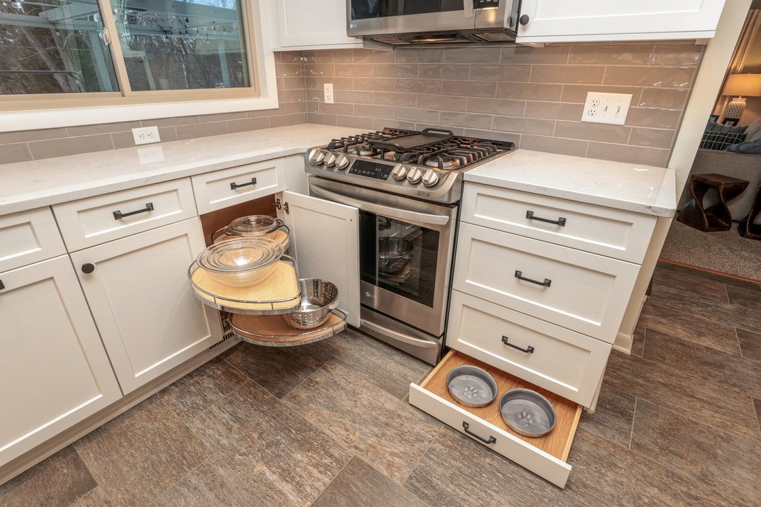A kitchen with white cabinets , stainless steel appliances , a stove and a drawer with plates in it.