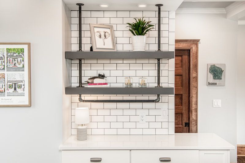 A kitchen with white cabinets , black pipe shelves , a picture on the wall and a plant on the shelf.