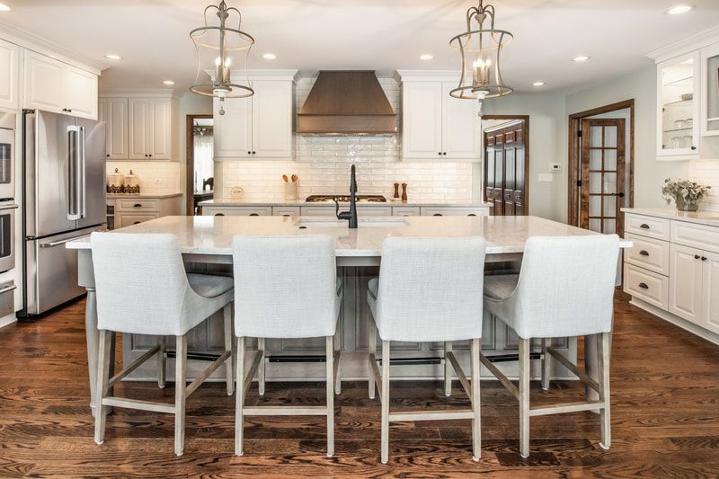 A kitchen with white cabinets , stainless steel appliances , hardwood floors and a large island.