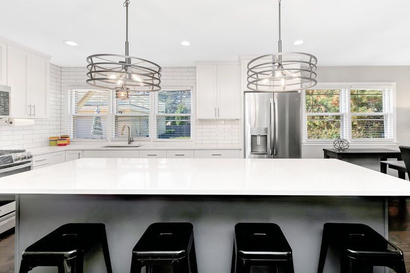 A kitchen with white cabinets , black stools and a large island.