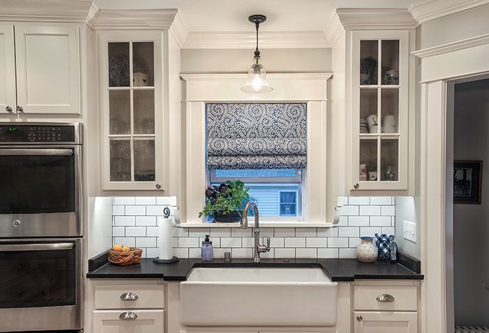 A kitchen with white cabinets , black counter tops , a sink and a window.
