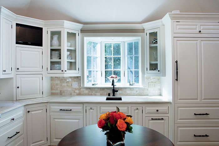 A kitchen with white cabinets and a table with a vase of flowers on it.
