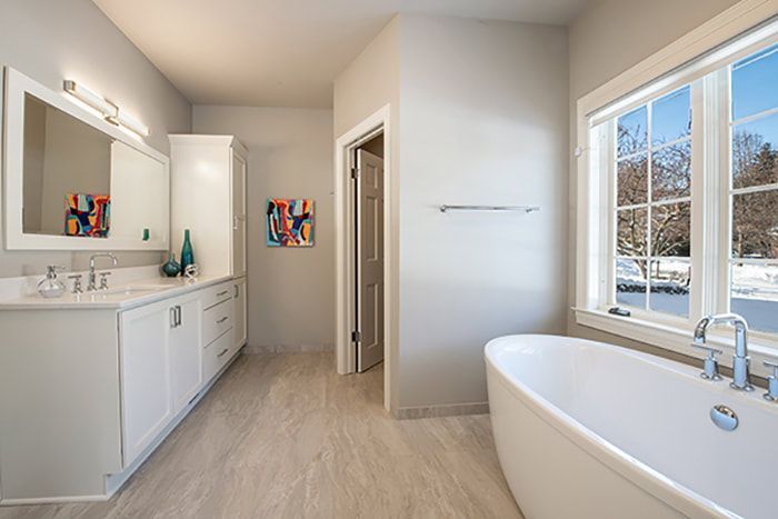 A bathroom with a tub , sink , mirror and window.