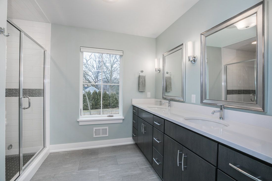 A bathroom with two sinks , two mirrors and a walk in shower.