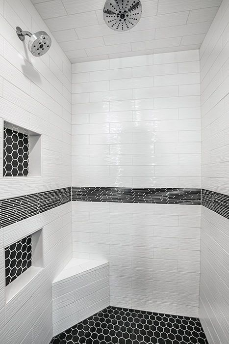 A shower with white tiles and black tiles and a shower head.