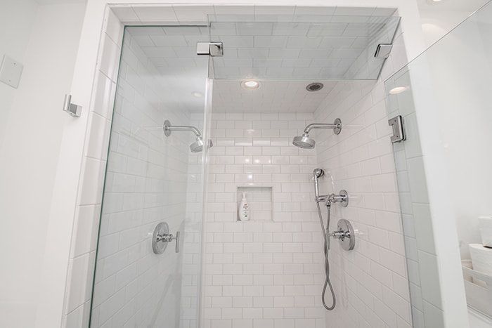 A bathroom with a walk in shower with two shower heads and a glass door.