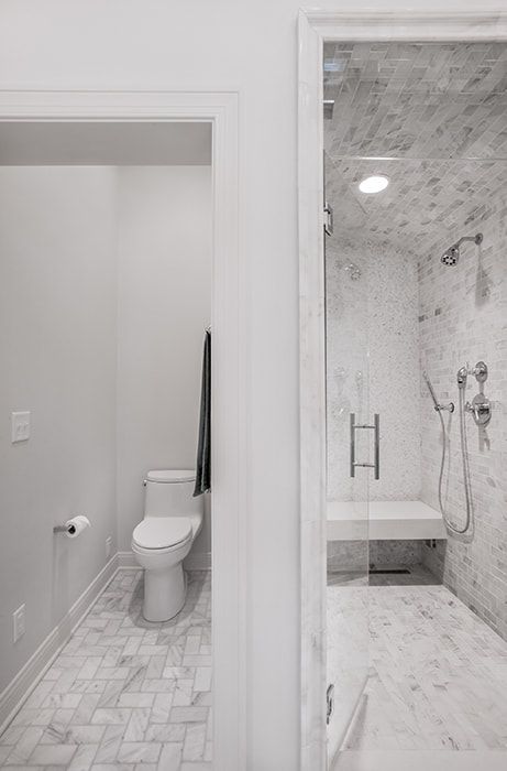A bathroom with a toilet , shower , and bench.