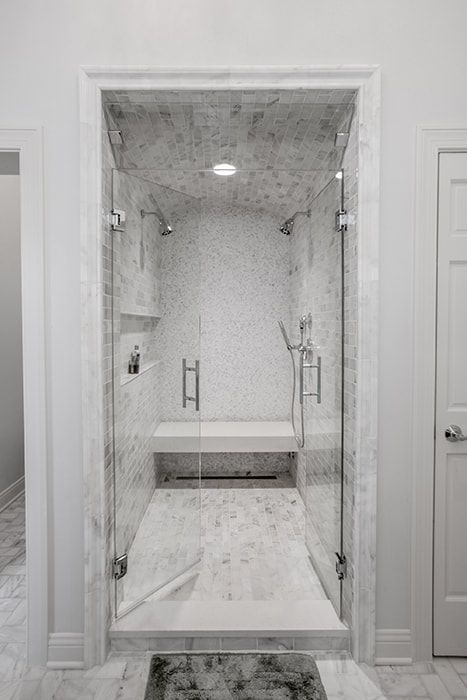 A bathroom with a walk in shower with a glass door and a bench.