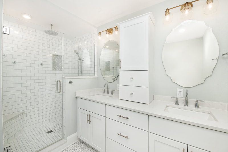 A bathroom with a walk in shower , sink , mirror and cabinets.