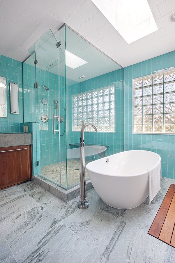 A bathroom with blue tiles , a tub , a shower and a skylight.