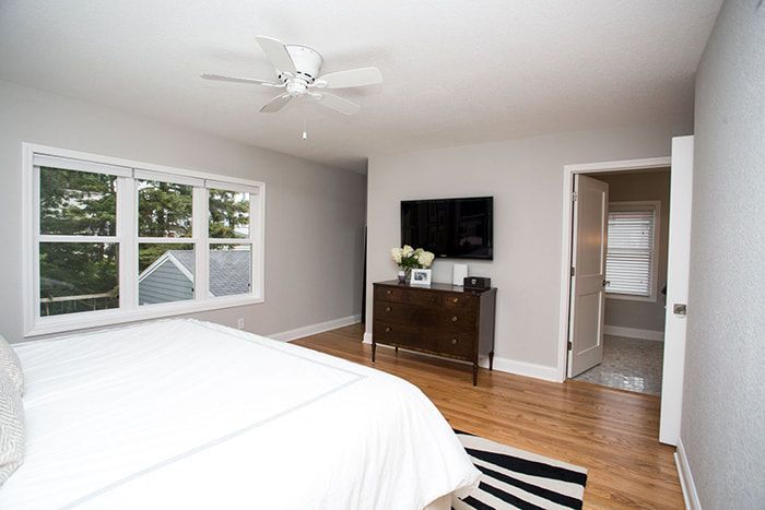 A bedroom with a bed , dresser , television and ceiling fan.